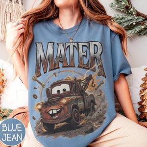 Puede incluir: Camiseta azul vaquero con un gr&aacute;fico de Mate de la pel&iacute;cula Cars. El dise&ntilde;o incluye la palabra "MATER" en una fuente desgastada sobre el cami&oacute;n de remolque de dibujos animados, con llaves y pernos alrededor de la imagen.