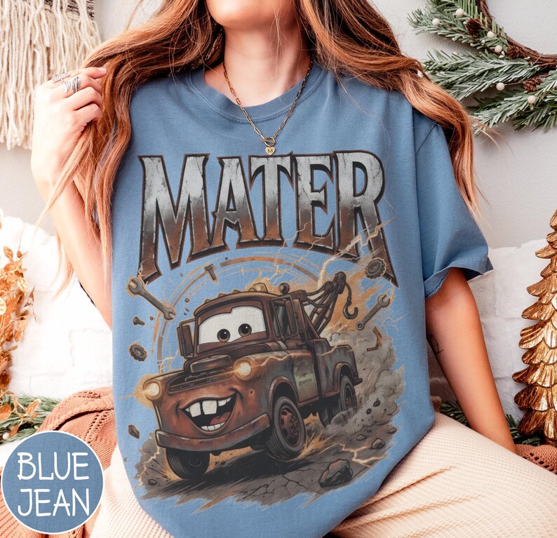 Puede incluir: Camiseta azul vaquero con un gr&aacute;fico de Mate de la pel&iacute;cula Cars. El dise&ntilde;o incluye la palabra "MATER" en una fuente desgastada sobre el cami&oacute;n de remolque de dibujos animados, con llaves y pernos alrededor de la imagen.