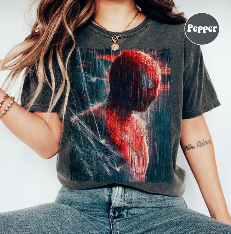 Pu&ograve; includere: T-shirt grigio scuro con una vivace illustrazione di Spider-Man in una scena piovosa. Il supereroe &egrave; raffigurato nel suo iconico costume rosso e blu, con gocce d'acqua e dettagli di ragnatela. La maglietta ha un aspetto vintage e usurato.