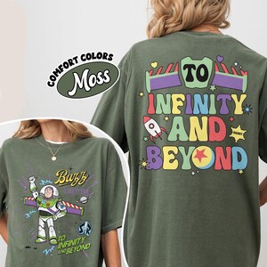 Op de afbeelding: Mosgroene t-shirts met Buzz Lightyear graphics. E&eacute;n shirt toont Buzz met de tekst "To Infinity and Beyond". Het andere shirt heeft de zin "To Infinity and Beyond" in kleurrijke letters met raket- en steraccenten.