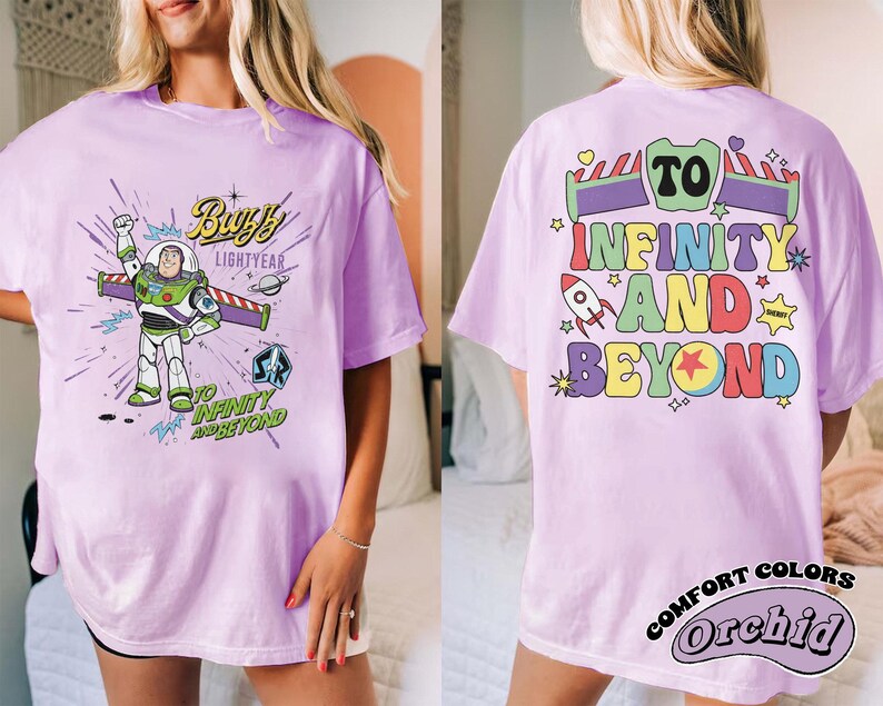 Op de afbeelding: Lila T-shirt met een Buzz Lightyear-afbeelding en de tekst "Buzz Lightyear" en "To Infinity and Beyond". De achterkant van het shirt toont "To Infinity and Beyond" in kleurrijke letters, een raket en sterren. Het shirt is een Comfort Colors Orchid.
