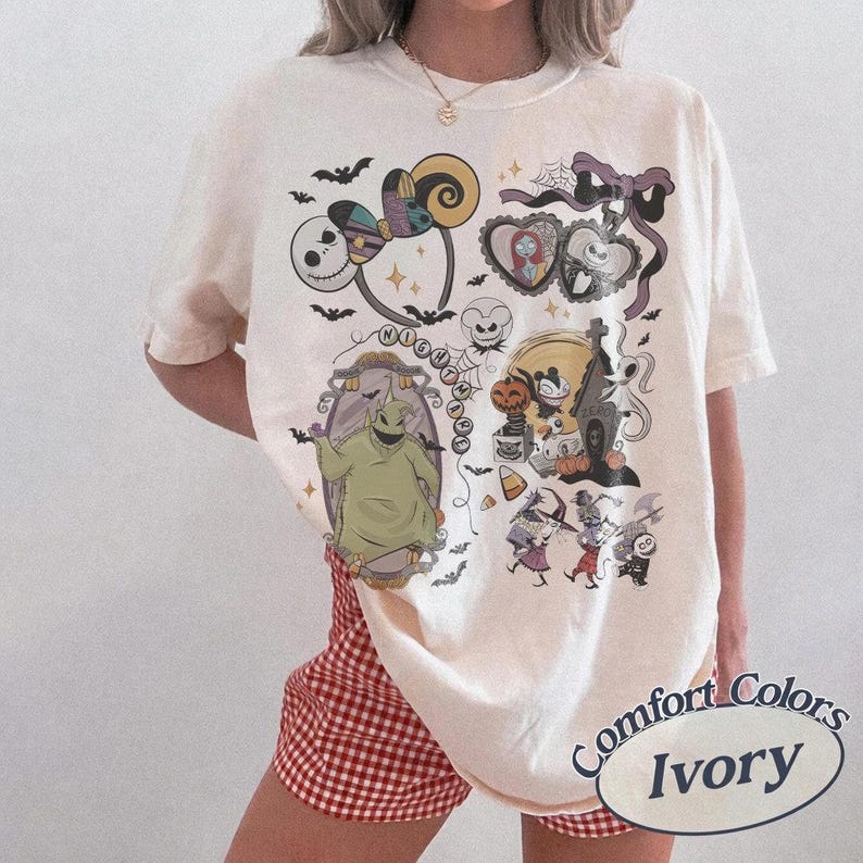May include: Ivory-colored t-shirt featuring a colorful graphic of characters and elements from "The Nightmare Before Christmas." The design includes Jack Skellington, Sally, Oogie Boogie, and other iconic imagery. The shirt is labeled "Comfort Colors Ivory."