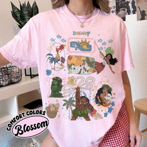 以下が含まれることがあります： ピンク色のComfort Colors Tシャツ。ディズニーのグラフィックで、映画モアナのキャラクターが描かれています。デザインには、ヘイヘイ、プア、ヘイヘイ、モアナ、マウイのイラストが含まれています。「Disney」の文字が上部に印刷されています。