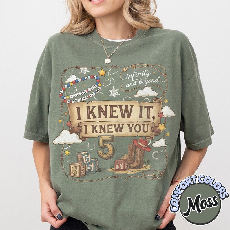 May include: A moss green short-sleeve t-shirt featuring a graphic print with a scroll banner reading I KNEW IT, I KNEW YOU, the number 5, cowboy boots, a hat, alphabet blocks, a beaded bracelet, and the text infinity and beyond.