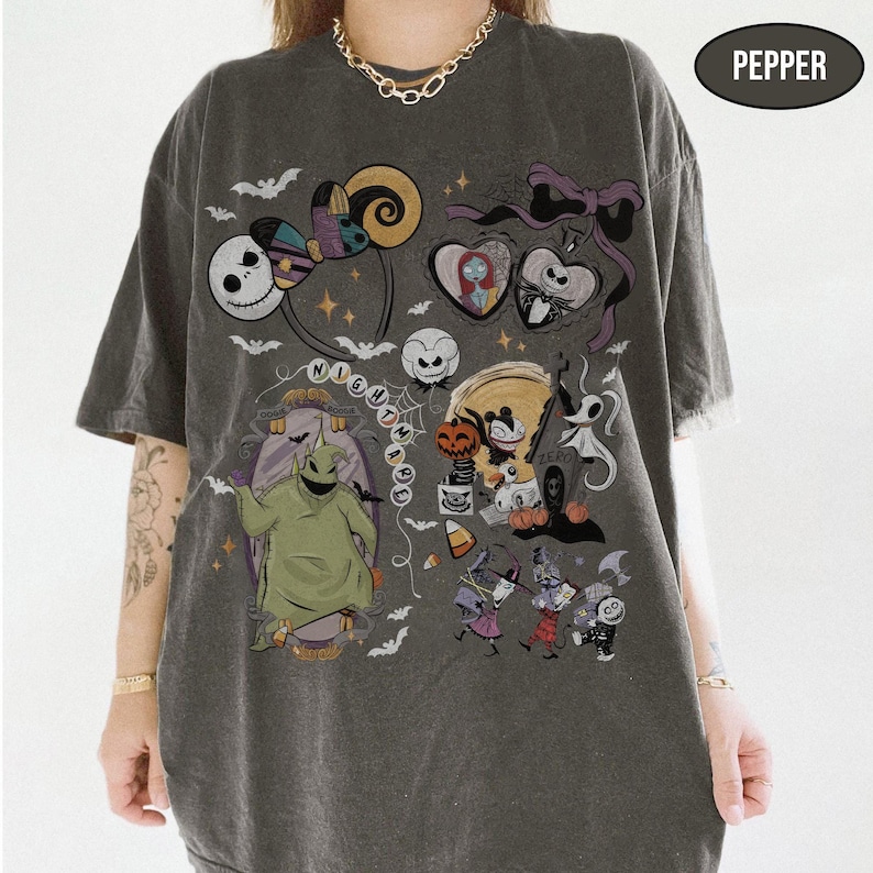 May include: Dark gray t-shirt featuring a colorful graphic design with characters and elements from the movie "The Nightmare Before Christmas." The design includes Jack Skellington, Sally, Oogie Boogie, and other iconic imagery. The word "NIGHTMARE" is also visible.