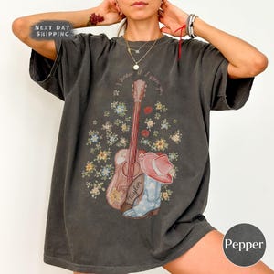 May include: A charcoal gray short-sleeve t-shirt featuring a graphic print of an acoustic guitar, a cowboy boot, and a cowboy hat surrounded by small colorful flowers. The text "I knew you" is printed in a curved arc above the guitar illustration.