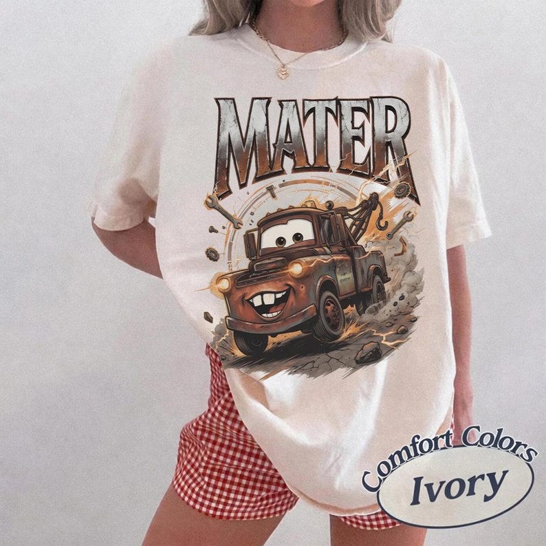 Puede incluir: Camiseta marfil Comfort Colors con una imagen de dibujos animados de Mate de la pel&iacute;cula Cars. El gr&aacute;fico incluye el nombre "MATER" en una fuente desgastada, un Mate sonriente y las palabras "Comfort Colors Ivory" en un dise&ntilde;o circular.