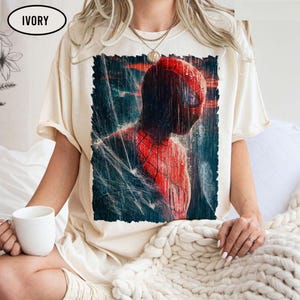 Pu&ograve; includere: T-shirt color avorio con grafica di Spider-Man sotto la pioggia. Il costume rosso e nero del supereroe &egrave; dettagliato, con un focus sulla sua maschera e sugli effetti dell'acqua. La maglietta ha una vestibilit&agrave; ampia.