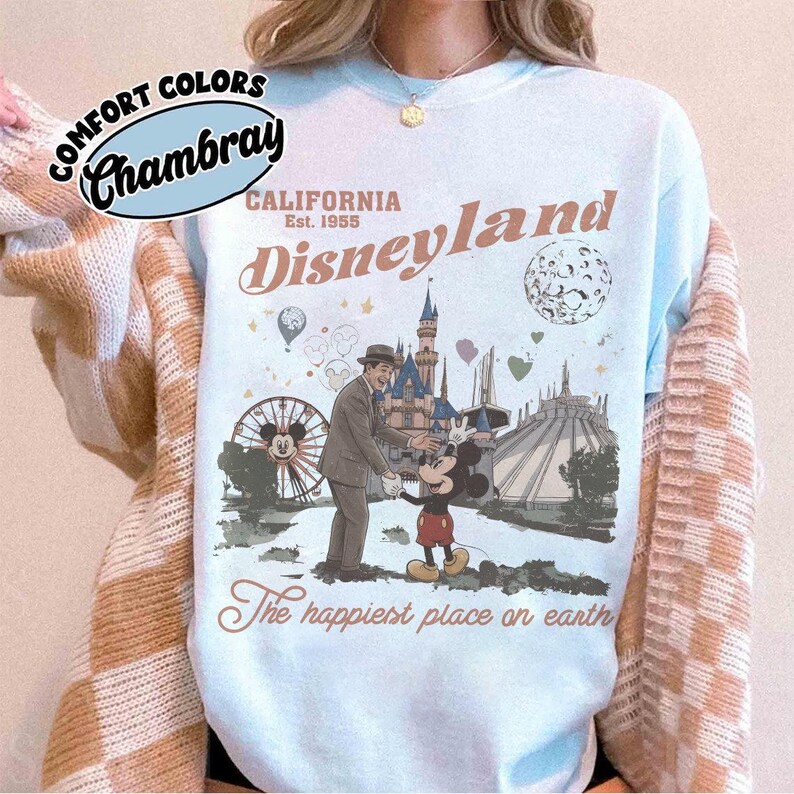Puede incluir: Sudadera azul claro de Disneyland con un gr&aacute;fico de estilo vintage. El dise&ntilde;o presenta a Mickey Mouse, un hombre con traje, una noria y el texto "Disneyland California Est. 1955" y "The happiest place on earth."