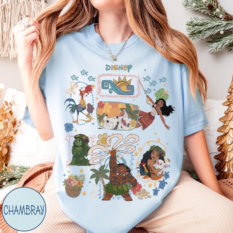 以下が含まれることがあります： ディズニーキャラクターが描かれた水色のTシャツ。モアナ、マウイ、ヘイヘイなどのキャラクターのカラフルなイラストが描かれています。「Disney」の文字が上部にプリントされています。丸首で半袖のTシャツです。