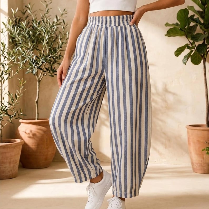 K&ouml;nnte beinhalten: Hoch taillierte Hose mit vertikalem blau-wei&szlig;em Streifenmuster. Die Hose hat eine weite Beinform, einen gerafften elastischen Bund und eine lockere Passform, die bis zu den Kn&ouml;cheln reicht, kombiniert mit einem schlichten wei&szlig;en bauchfreien Oberteil.