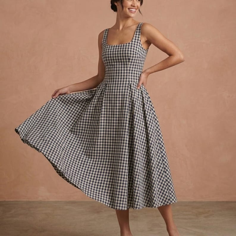 May include: A sleeveless midi dress featuring a black and white gingham check pattern. The dress has a square neckline, a fitted bodice, and a full, flared skirt that falls below the knees. The design includes wide shoulder straps and a defined waistline.