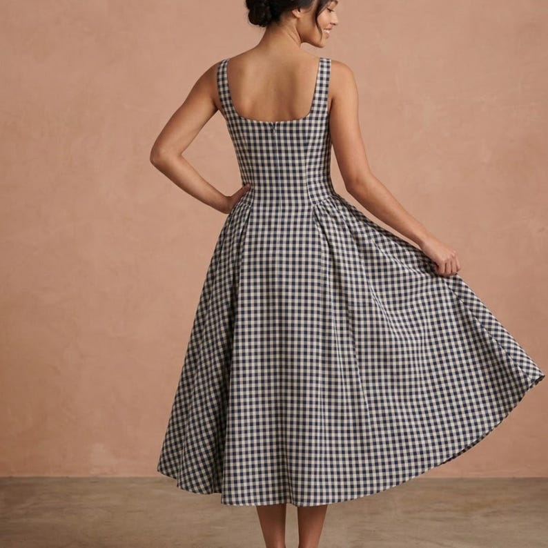 May include: A sleeveless midi dress featuring a black and white gingham check pattern. The dress has a square neckline, a fitted bodice, and a full, pleated skirt that flares out from the waist, creating a structured and voluminous silhouette.