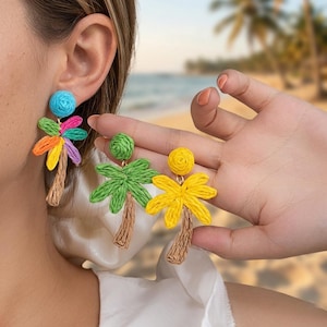 Puede incluir: Pendientes de palmera hechos a mano en colores vibrantes. Un pendiente tiene un perno azul y frondas arcoíris, el otro tiene frondas verdes y amarillas. Los troncos son de color marrón tejido. Un accesorio divertido y tropical.
