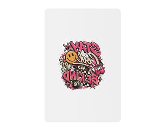 May include: A white rectangular surface featuring a central graphic design with the text STAY COOL AND BE KIND in pink and black. The illustration includes a yellow smiley face, a black eight ball, dice, cherries, a flower, and stars.