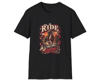 May include: A black short-sleeve t-shirt featuring a graphic print of a horse running through a desert landscape with cacti and a sunset. The text RIDE YOUR OWN WAY is printed in white and red lettering, accompanied by a cowboy hat and horseshoe.