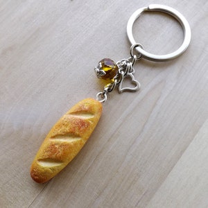 May include: A yellow baguette keychain with a silver charm and a clear amber bead. The keychain is attached to a silver key ring.