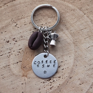 Könnte beinhalten: Ein silberner Schlüsselanhänger mit einem Kaffeebohnen-Anhänger, einem kleinen silbernen Kaffeekannen-Anhänger und einem silbernen Anhänger mit dem Text "COFFEE TIME" und einem Herz.