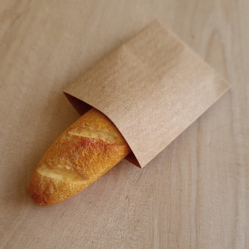 May include: A brown paper bag with a crusty baguette inside.
