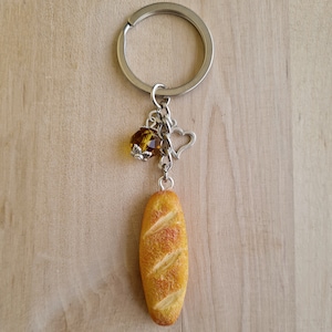 May include: A silver keychain with a small, yellow crystal charm, a heart charm, and a charm shaped like a loaf of bread.