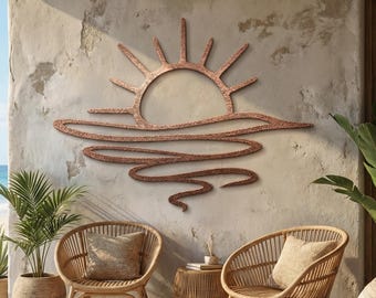 May include: A copper-colored metal wall art piece depicting a sun setting over the ocean. The artwork is mounted on a textured, light-colored wall, with outdoor furniture and plants in the foreground. The sun's rays extend upwards.