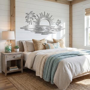 May include: A silver-colored metal wall art piece featuring a stylized sun rising over a horizon with palm trees on both sides and a rippled water effect below. The design is flat, cut from metal, and displays a coastal landscape scene.