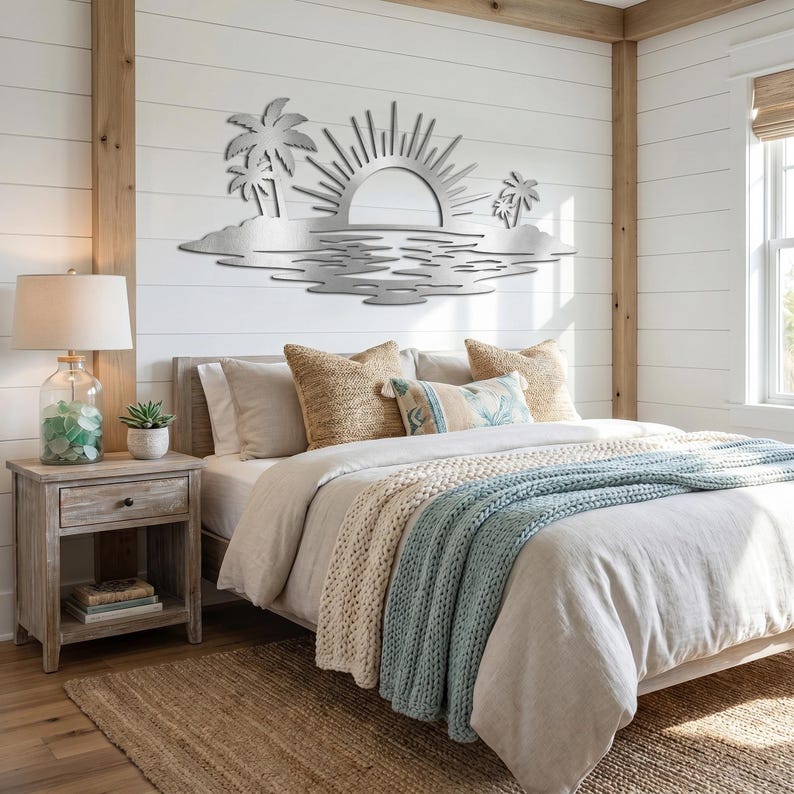 May include: A silver-colored metal wall art piece featuring a stylized sun rising over a horizon with palm trees on both sides and a rippled water effect below. The design is flat, cut from metal, and displays a coastal landscape scene.