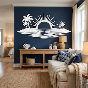 May include: A white wall art piece featuring a stylized sun rising over a tropical island with palm trees and water reflections, mounted on a dark blue wall above a wooden console table in a living room setting with a sofa and lamps.