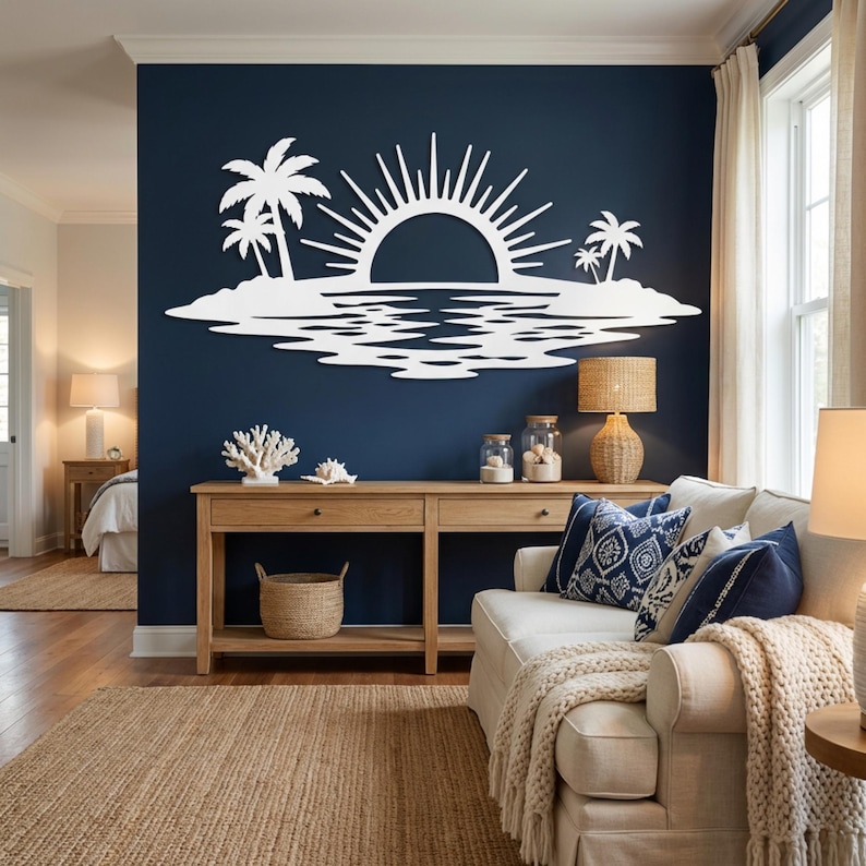 May include: A white wall art piece featuring a stylized sun rising over a tropical island with palm trees and water reflections, mounted on a dark blue wall above a wooden console table in a living room setting with a sofa and lamps.