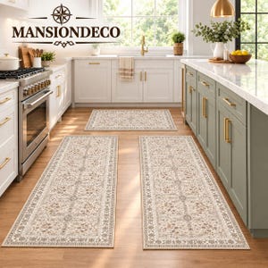 May include: A set of three rectangular kitchen rugs featuring a cream-colored base with intricate floral and geometric patterns in shades of brown, tan, and gray. The rugs have a decorative border and are placed on a light wood floor in a kitchen.