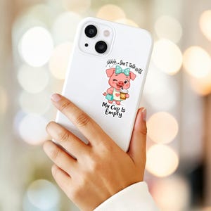 May include: White phone case with a cartoon pig illustration. The pig is pink with a blue bow, holding a coffee cup and a purse. Text on the case reads "shhhh... Don't Talk until My Cup Is Empty."