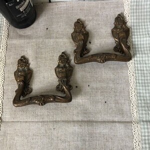 Può includere: Due tiretti per cassetti in ottone antico decorati con un motivo a volute. I tiretti hanno una maniglia ad anello e sono in ottime condizioni.