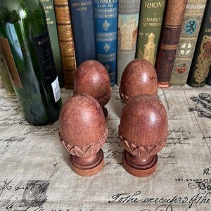 May include: Four carved wooden finials with a smooth, rounded top and a decorative leaf-like base. Each finial features a warm, reddish-brown wood grain finish and stands on a circular pedestal base. The objects are arranged in a square formation.
