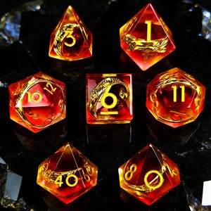 Può includere: Set di sette dadi poliedrici con una sfumatura arancione e gialla infuocata. Ogni dado presenta dettagli dorati e numeri gialli. I dadi sono progettati per giochi di ruolo da tavolo.