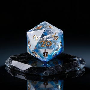 May include: A twenty-sided die with a marbled blue and white design, featuring gold-colored numerals. The die is resting on a dark, reflective surface, creating a dramatic contrast against the black background. A unique gaming accessory.