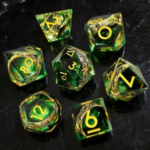 Puede incluir: Conjunto de siete dados poliédricos verdes y dorados. Cada dado presenta números dorados y filigranas doradas decorativas dentro de la resina verde transparente. Los dados están diseñados para juegos de rol de mesa.