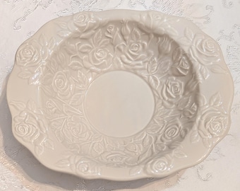 May include: An off-white ceramic bowl featuring a raised, embossed floral pattern of roses and leaves covering the wide rim and extending into the interior basin. The bowl has a smooth, glossy finish and a scalloped edge design throughout its perimeter.