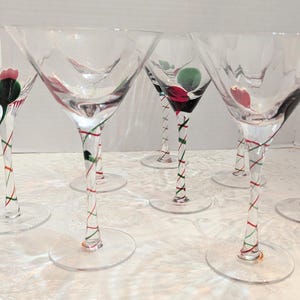 Könnte beinhalten: Ein Set aus sechs klaren Martini-Gläsern aus Glas mit breiten, konischen Kelchen. Jeder Stiel weist ein zartes, spiralförmiges Design aus roten und grünen Glasfäden auf, mit einem kleinen, farbigen Glasakzent am Kelchansatz in Rosa, Grün und Schwarz.
