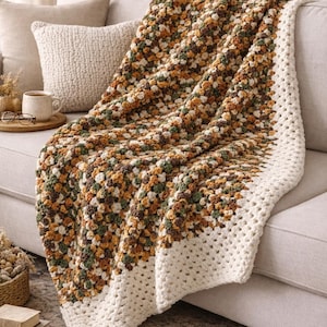 Op de afbeelding: Handgemaakte, gezellige gehaakte sprei in een mix van bruin, groen en wit. De deken is over een bank gedrapeerd, met de woorden "HANDMADE COZY CROCHET THROW" onderaan.