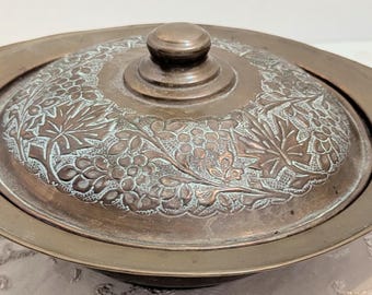 Ciotola vintage Arts & Crafts in rame con coperchio, decorazione a rilievo a tralci di vite, casseruola con manici e patina rustica.
