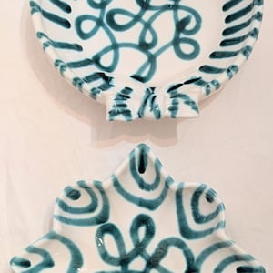 May include: Two white ceramic dishes with hand-painted teal blue patterns. The top dish is round with bow-shaped accents and a central swirling design. The bottom dish is star-shaped with six points and a matching central swirling teal pattern.