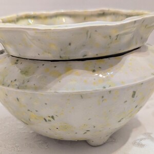May include: A two-piece ceramic planter with a glossy white glaze featuring speckled yellow and green accents. The design includes a wide, scalloped-edge top basin that rests inside a rounded, footed base, creating a layered, organic silhouette.