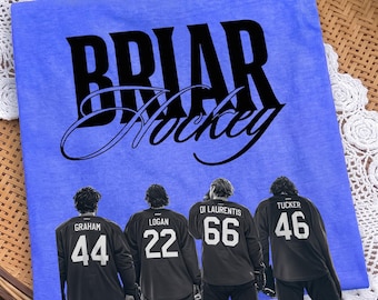 May include: A periwinkle blue t-shirt featuring the black text BRIAR Hockey above a graphic of four hockey players wearing black jerseys with the names and numbers Graham 44, Logan 22, Di Laurentis 66, and Tucker 46 printed on the back.