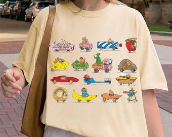 May include: A cream-coloured short-sleeve t-shirt featuring a graphic print of various cartoon animals driving whimsical vehicles shaped like food items, a toothbrush, and a tube of toothpaste, with the text Mistress Mouse Repairs and Pickles.