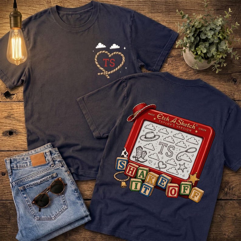 May include: A dark blue t-shirt featuring a rope heart with the letters TS on the front chest. The back displays a red Etch A Sketch toy with the text Taylor's Version, surrounded by cowboy boots, hats, and blocks spelling SHAKE IT OFF.