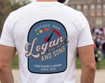 May include: A white t-shirt featuring a blue graphic on the back. The design includes a speedometer gauge, the text "Hastings, Mass.", "Logan AND SONS", "MECHANIC & REPAIR SHOP", and "MAINTENANCE & REPAIRS SINCE 1975" in a mix of script and block lettering.