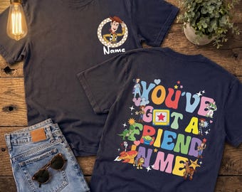 May include: A dark navy blue t-shirt featuring a small circular graphic on the front chest with a cowboy character and the word Name. The back displays a large colourful graphic with the text You've Got A Friend In Me and various characters.