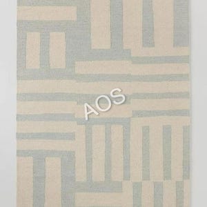 May include: Rectangular rug with a geometric pattern. The rug features a repeating design of light blue and off-white rectangular shapes. The rug is made of a soft, textured material, and the overall design is modern and minimalist.