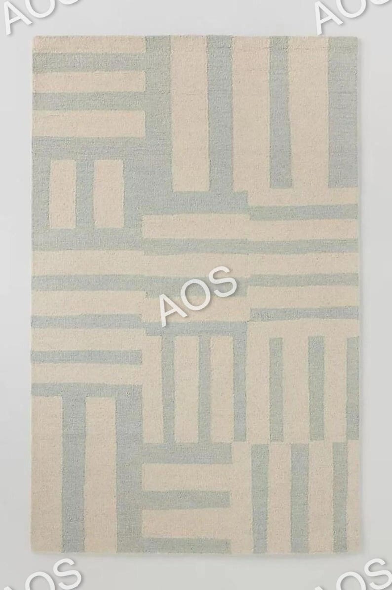 May include: Rectangular rug with a geometric pattern. The rug features a repeating design of light blue and off-white rectangular shapes. The rug is made of a soft, textured material, and the overall design is modern and minimalist.