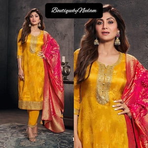 May include: Mustard yellow salwar kameez with gold embroidery and a pink and gold patterned dupatta. The outfit features a round neckline and three-quarter sleeves. The text "BoutiquebyNeelam" is in the upper left corner.